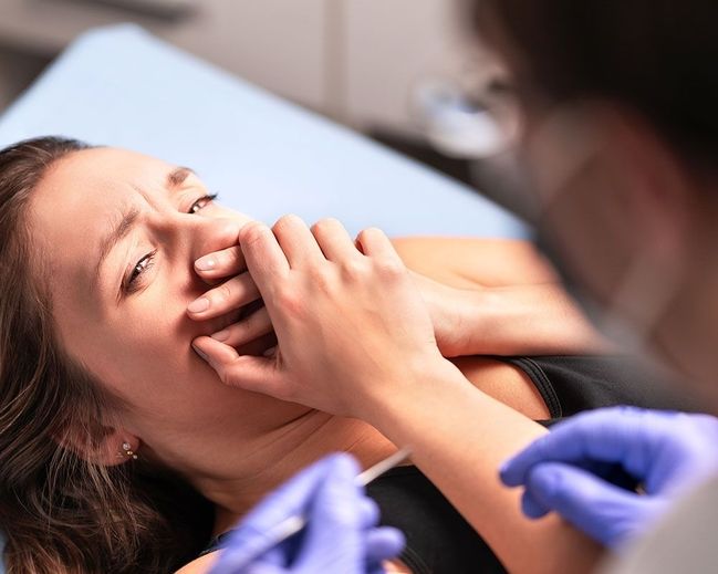 Junge Frau zeigt starke Zahnarztangst und verdeckt verängstigt den Mund