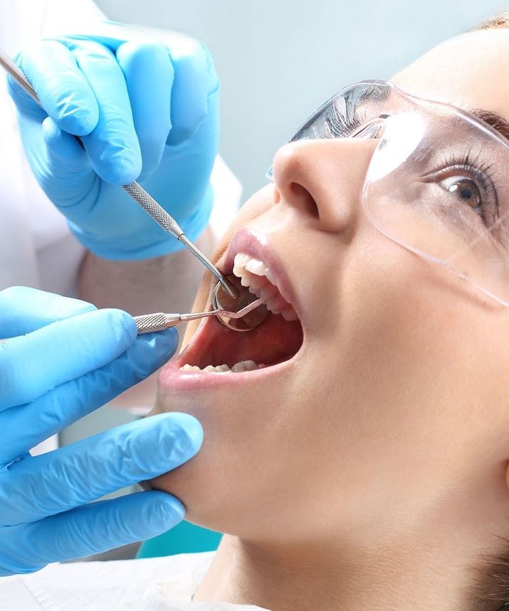 Zahnärztliche Untersuchung bei einer jungen Frau mit Schutzbrille und geöffnetem Mund