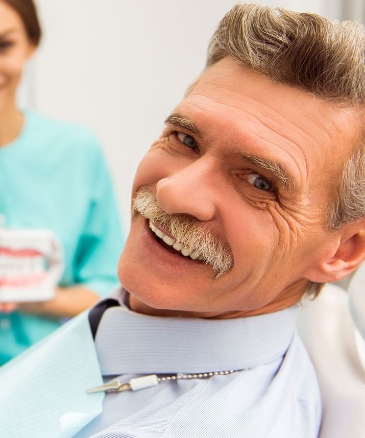 Lächelnder älterer Patient im Zahnarztstuhl, Blick in die Kamera